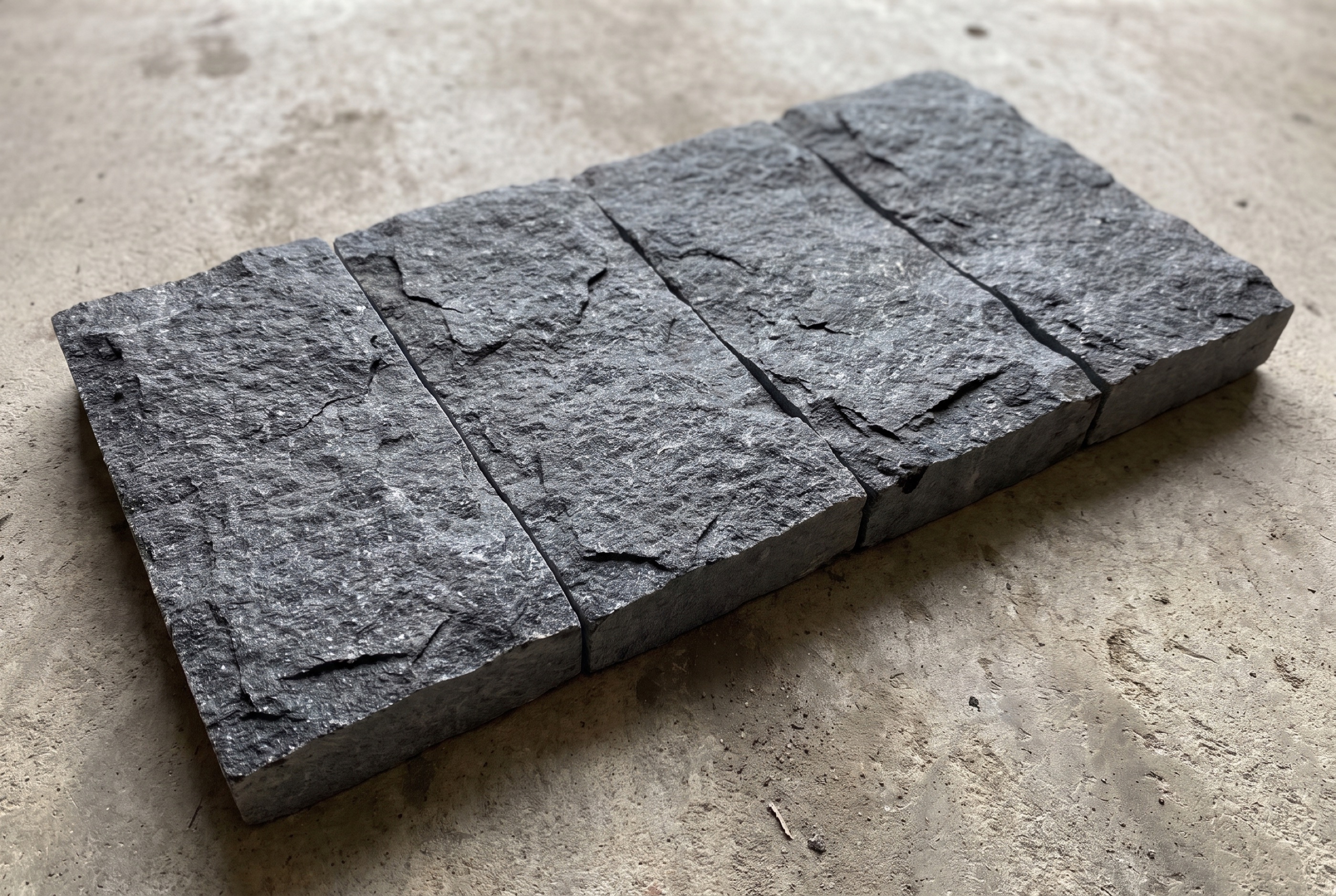 Four Black Ice L7 splitface granite pavers lying on concrete